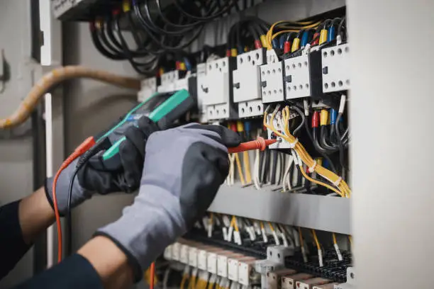 Technician inspecting corroded panel connections with meter and insulated tools
